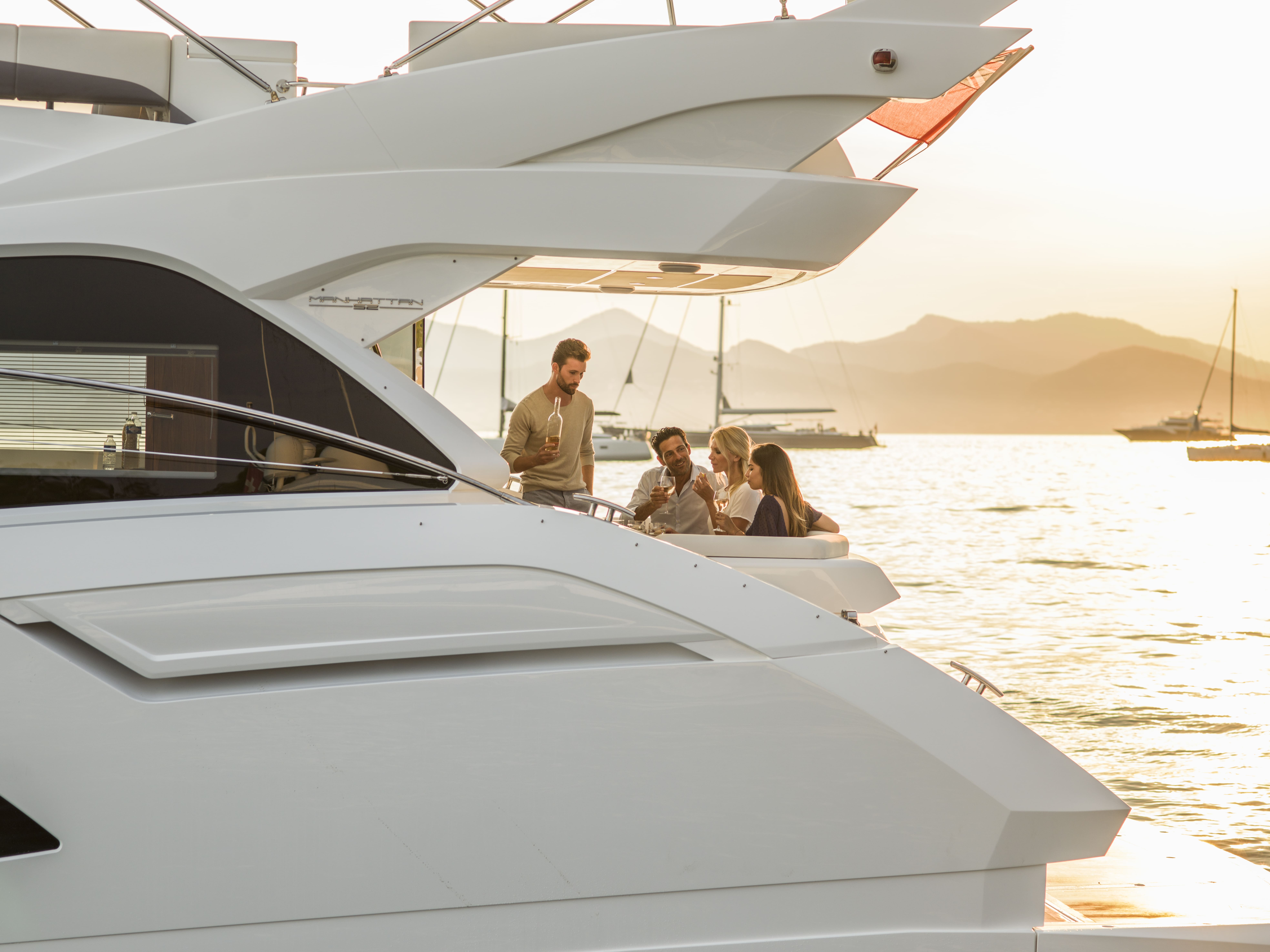 Four people relaxing on the rear deck of a yacht at sunset in a marina