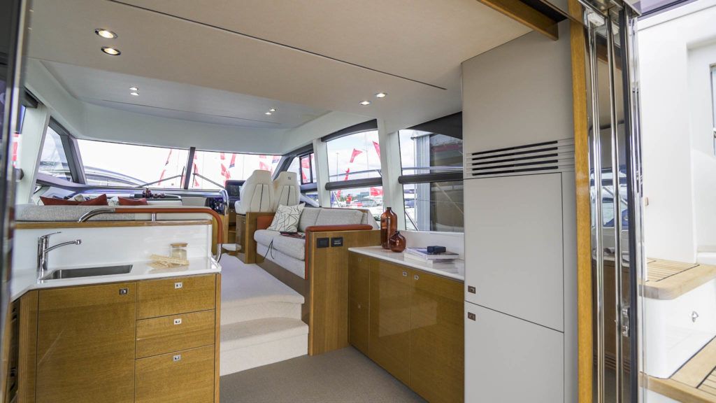 Yacht interior from the perspective of a yacht kitchen, looking towards the helm, with a mixture of cream fabrics and burnt orange accents