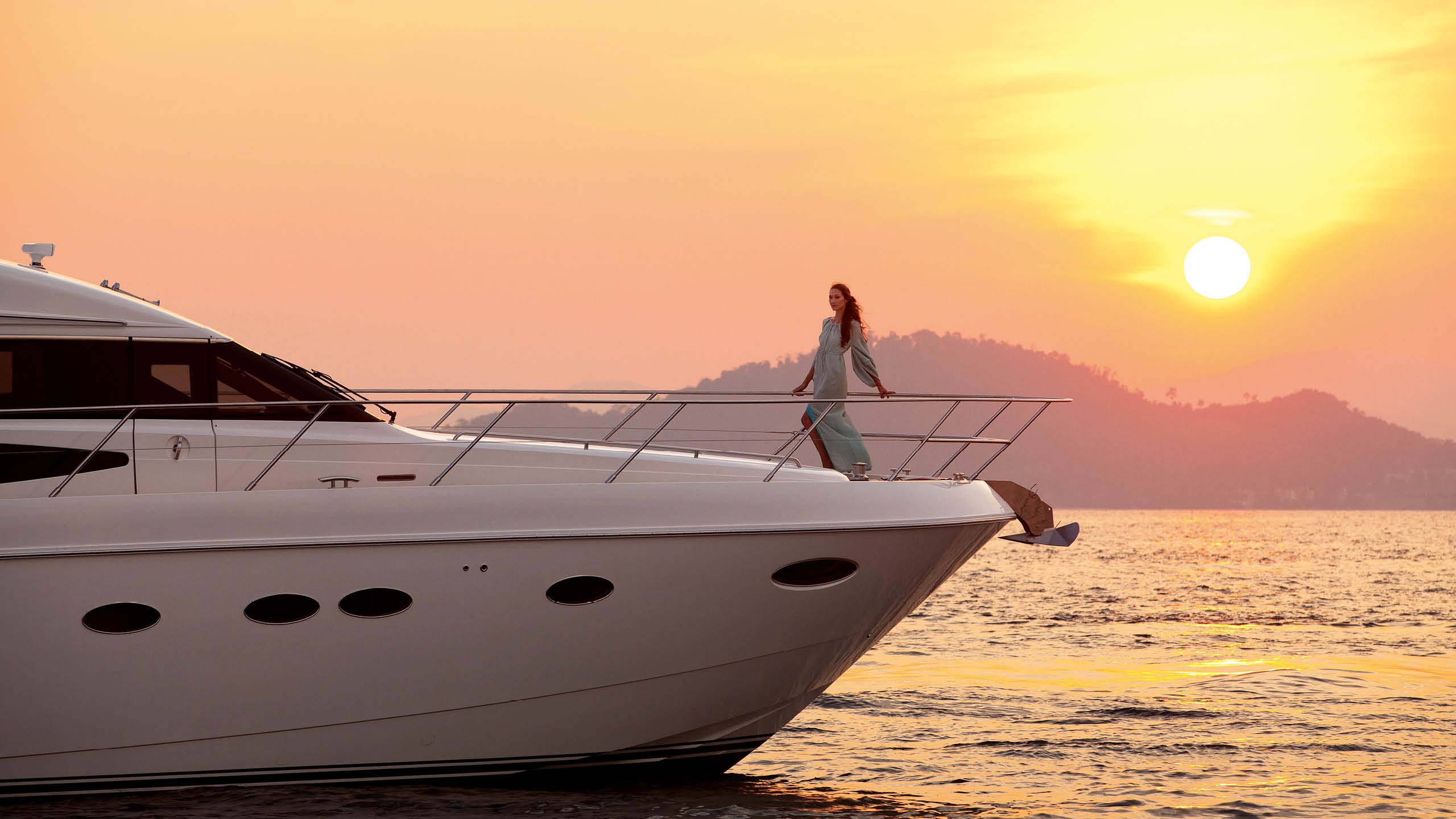 Lady standing on the deck of a sailing yacht with a sunset in the background